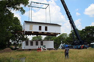 A crane lifts the second story off of a white clapboard house