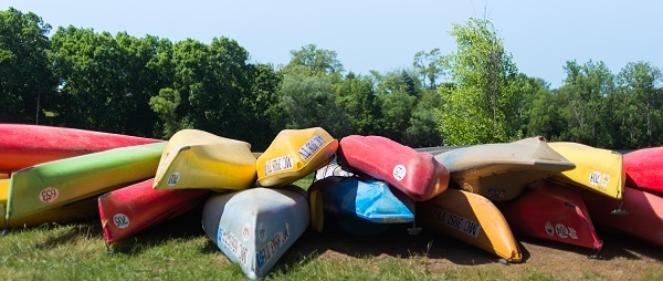 a pile of colorful canoes, upside down, on the grass, blue sky behind
