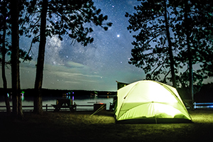 tent on wooded campsite by lake at night