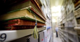 A stack of ledgers sits on a shelf in an archival storage room. 