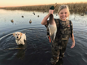 young female waterfowl hunter, with dog, holding harvested duck