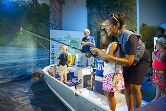 Mother helps girl use fishing simulator at OAC