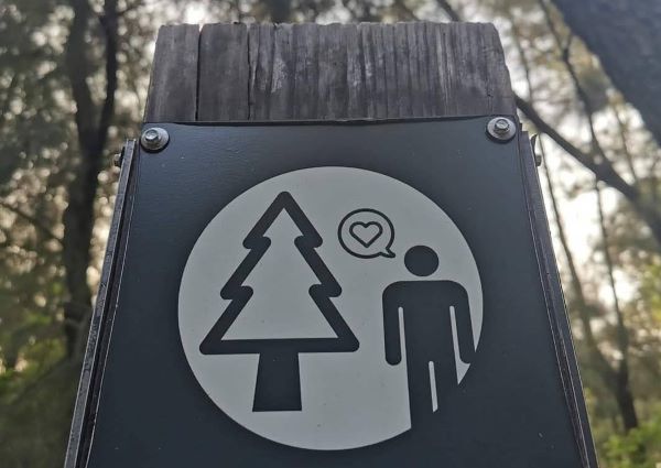 Image of a trail sign with a person, a tree, and a heart