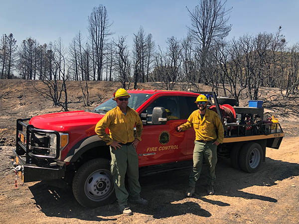 Two Michigan DNR firefighters are shown standing in front of their truck out west.