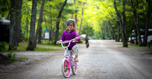 A young girl wearing glasses rides a bicycle on a tree-lined path