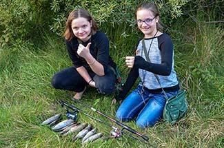 Two girls are shown giving a thumbs-up sign as they display a limit brook trout catch.