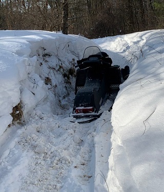 view of a snowmobile partially buried under snow on a trail in the forest