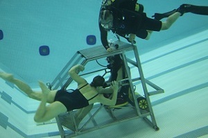 a woman in a swimsuit practices underwater rescue from a submerged vehicle while a SCUBA-clad instructor watches