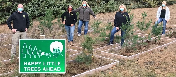 A group of people plant trees near a "happy little trees" sign