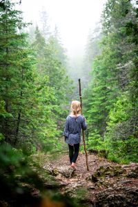 A young girl hikes in a forest with a walking stick