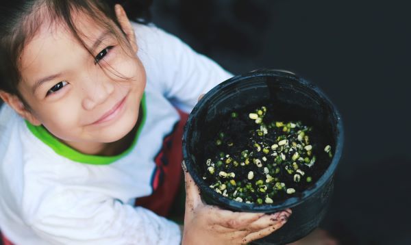 A young girl holds a pot full of sprouting seeds