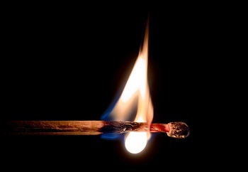 close-up view of a lit match, held horizontally, against a black background