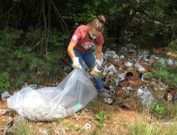 female volunteer in face mask picks up garbage in forest