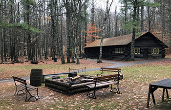 Hartwick Pines Logging museum cook fire and log cabin in background in the autumn