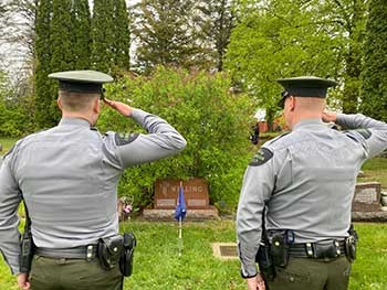 Two Michigan conservation officers salute at the grave of a fellow officer.