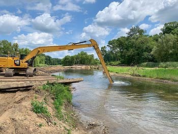 An excavator operator digs a bucket into the Dowagiac River to dig the pilot course for the water behind the dam.