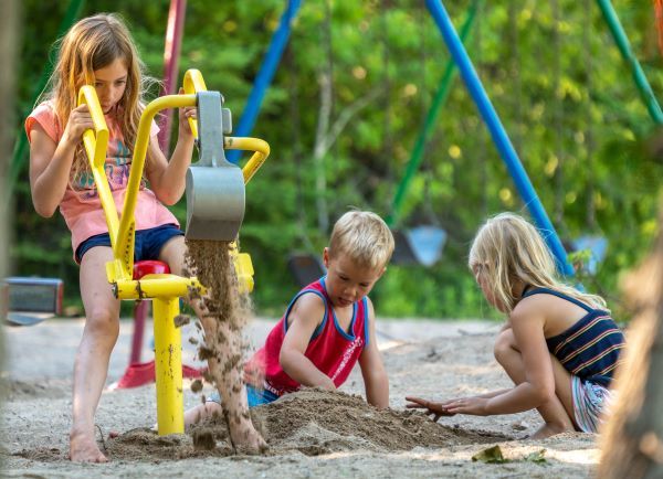 Three young children play with toys in the sand at the Straits State Park playground