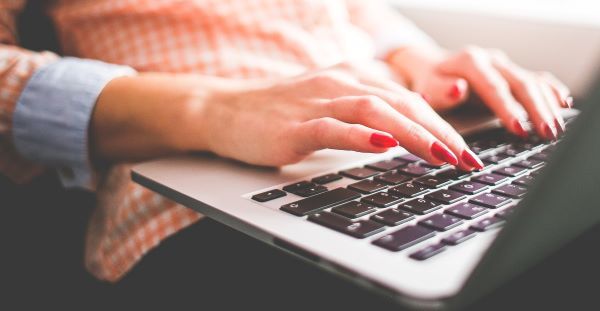 A laptop computer rests on a person's legs, with hands ready to type.