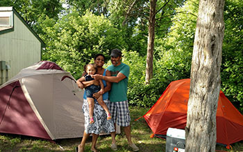 parents holding baby in front of tent and camper cabin