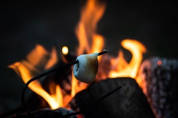 nighttime photo of a melty marshmallow hanging off a stick, over a glowing orange campfire