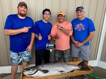 Four men, some wearing baseball caps, pose with a new state-record Chinook salmon on a scale