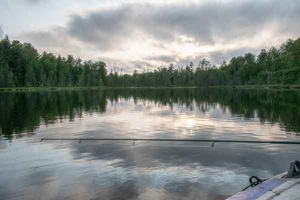 This image shows a remote U.P. trout lake with a fishing rod perched on the side of a raft. 