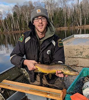 A DNR fisheries technician holds a large brown trout in a boat on a survey of a U.P. trout lake.