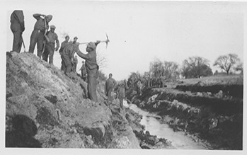 Several men in uniform stand on and atop a steep embankment down to a small stream.