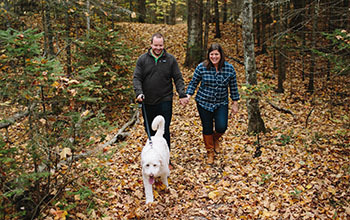 man and woman walking with dog on trail with fall leaves