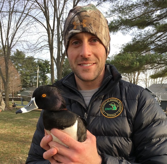 Wildlife biologist, Jeremiah Heise, smiles and holds a lesser scaup duck.