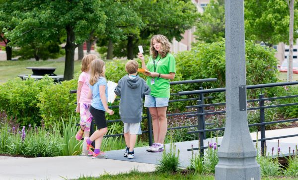 An instructor speaks to three children in a summer, outdoor setting 