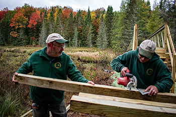 Two DNR workers cut a piece of wood for an elevated boardwalk at Craig Lake State Park.