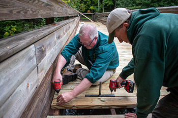 Two Michigan DNR workers improve decking on a walkway bridge at the Bond Falls Scenic Site.