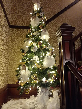 A Christmas tree with cream lights, feathers and ornaments is displayed on a staircase landing.