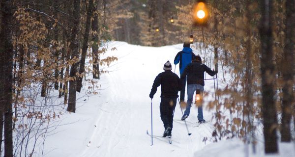 A group of three skiiers enjoy a lantern-lit winter trail