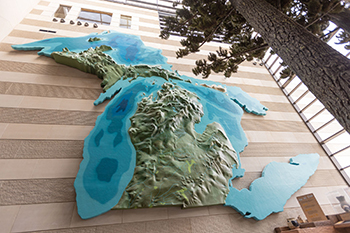 A three-story relief map of Michigan and the Great Lakes is mounted on a stone wall. 