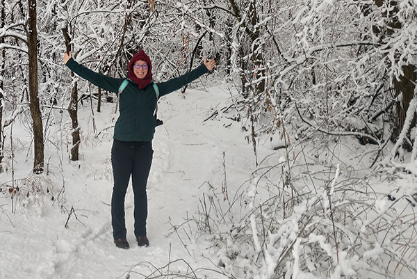 The author is shown raising her hands toward the sky in a snowy woodland.