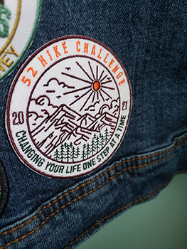 A 52 hikes embroidered commemorative patch is shown stitched into a denim jacket.