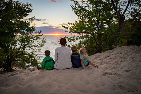 Mom and three young kids sitting on beach watching sunset