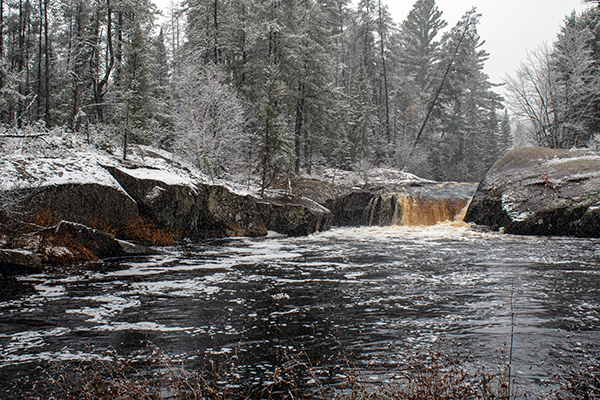 An Upper Peninsula waterfall tumbles over rocks in a snow-covered Marquette County scene.