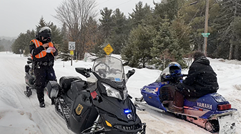 A conservation officer is shown at a snowmobile traffic stop with a rider in Marquette County.