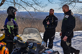 Two snowmobile club members talk with a DNR trails official while on a snowmobile ride in Gogebic County.
