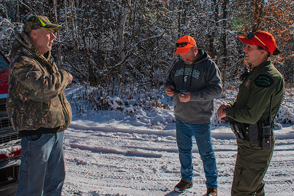 A conservation officer checks hunting licenses of two men on a snowy November day in Iron County.