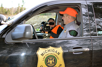 A conservation officer seated in his patrol vehicle is being filmed for an episode of "Wardens."