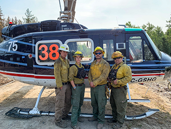 DNR firefighters pose for a photo next to a helicopter while on assignment in Manitoba.