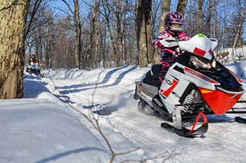 Two snowmobilers ride along a trail in Marquette County on a sunny afternoon.