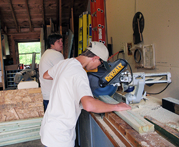 Two Michigan Rehabilitation Services enrollees are shown working on a lumber cutting project.