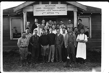 A group of land surveyors involved in mapping Michigan are shown in front of a surveying office in a historic group photo.