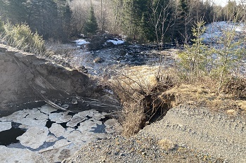 A view of the partially washed out embankment and berm surrounding an earthen dam, with mucky water several feet down
