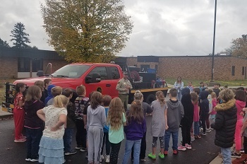A DNR firefighter stands outside his red truck talking with a large group of kids at a school in Gladwin, Michigan.